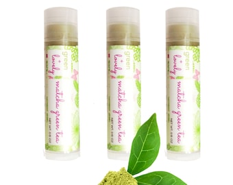 Könnte beinhalten: Drei Lippenbalsam-Tuben mit dem Text "green + lovely matcha green tea" werden angezeigt. Ein Haufen grünes Pulver und zwei grüne Blätter befinden sich vor den Tuben. Jede Tube ist mit "NET WT. 0,15 OZ." beschriftet.