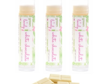 May include: Three lip balm tubes and white chocolate pieces. The lip balm tubes are white with green and pink text that reads "green + lovely white chocolate." The white chocolate pieces are arranged in a pile.