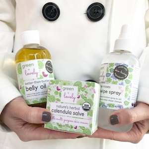May include: Three Green + Lovely baby care products: belly oil, calendula salve, and wipe spray. The belly oil is in a clear bottle, the salve in a green and white box, and the wipe spray in a clear spray bottle. All products have floral and bird designs.