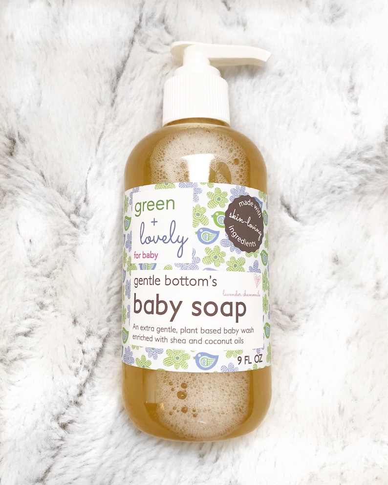May include: A clear plastic bottle of baby soap with a white pump dispenser. The label reads "green + lovely for baby" and "gentle bottom's baby soap." The bottle contains a light brown liquid and is 266 ml.
