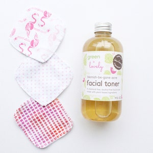 May include: A clear bottle of facial toner with a silver cap and a label that reads "green + lovely blemish-be-gone acne facial toner." Three reusable facial pads with pink patterns are next to the bottle. The bottle contains 9 fl oz of toner.