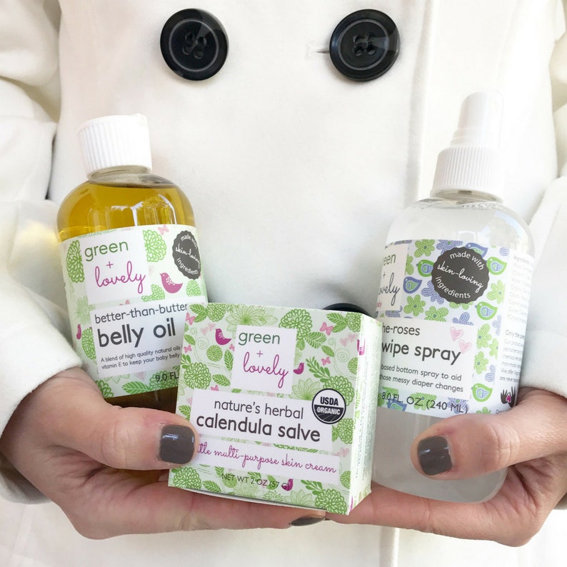 May include: A collection of baby care products, including a bottle of belly oil, a box of calendula salve, and a wipe spray. The products are labeled "green + lovely" and feature floral and bird designs. The belly oil bottle is 9.0 fl oz.
