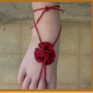 Könnte beinhalten: Rotes gehäkeltes Fußkettchen mit Blumenmuster. Das Fußkettchen ist um den Knöchel gebunden und hat eine lange Schnur, die das Bein hinaufgeht.