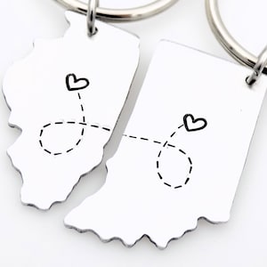 May include: Two silver keychains shaped like the states of Illinois and Indiana, connected by a dotted line with hearts at each end.