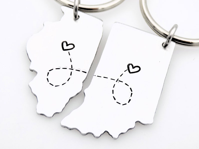May include: Two silver keychains shaped like the states of Illinois and Indiana, connected by a dotted line with hearts at each end.