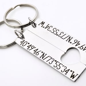 May include: A silver keychain with two key rings and a rectangular tag. The tag is split into two sections, each with a set of coordinates engraved on it. The coordinates are 40&deg;49&prime;46&Prime;N/73&deg;55&prime;34&Prime;W. The tag has a heart-shaped cutout in the middle.