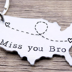 May include: Silver keychain shaped like the United States with a dotted line across the middle and two small hearts. The text "Miss you Bro" is engraved on the keychain.