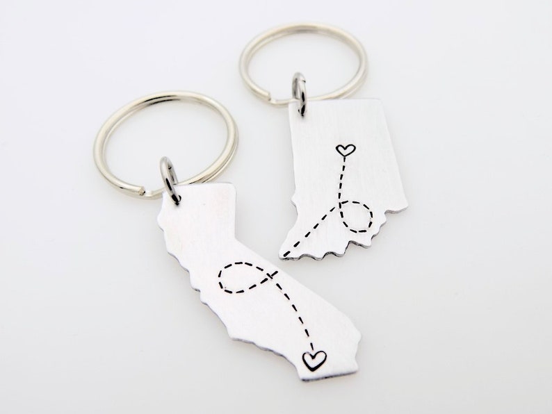 May include: Two silver keychains featuring the outlines of Indiana and California. A dotted line with hearts connects the two states.