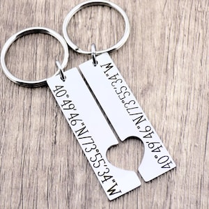 May include: Two silver keychains with heart-shaped cutouts. Each keychain has a rectangular tag with engraved coordinates: 40&deg;49&prime;46&Prime;N/73&deg;55&prime;34&Prime;W.