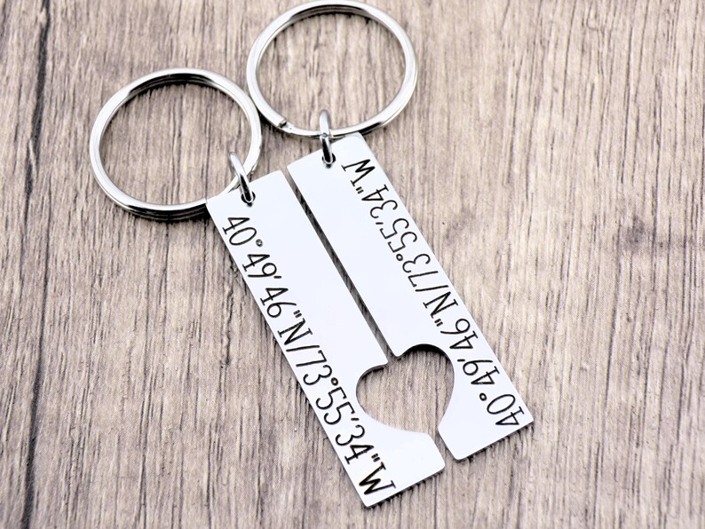 May include: Two silver keychains with heart-shaped cutouts. Each keychain has a rectangular tag with engraved coordinates: 40&deg;49&prime;46&Prime;N/73&deg;55&prime;34&Prime;W.