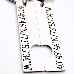 May include: Two silver keychains with a heart-shaped cutout. Each keychain has a rectangular tag with coordinates engraved on it. The coordinates are 40&deg;49&prime;46&Prime;N/73&deg;55&prime;34&Prime;W.