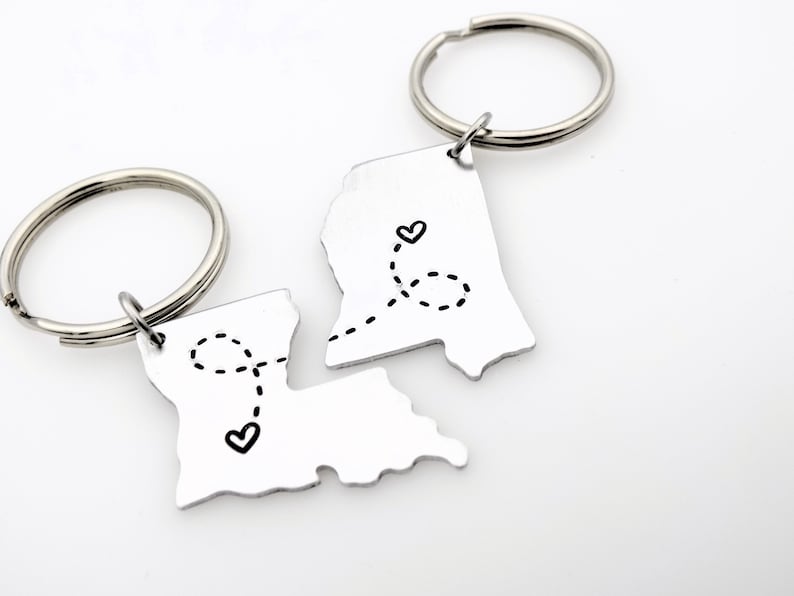 May include: Two silver keychains shaped like the state of Louisiana, each with a heart and a dotted line connecting them. The keychains are separated, suggesting a long-distance relationship.
