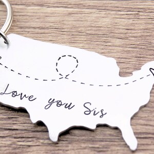May include: Silver keychain shaped like the United States with a dashed line connecting two hearts and the text "Love you Sis".