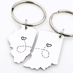 May include: Two silver keyrings with a heart and a dotted line connecting the outlines of the states of Illinois and Indiana.