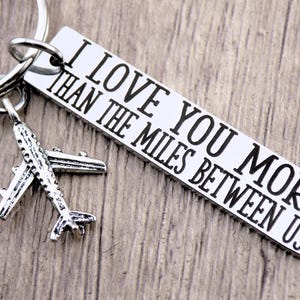 May include: Silver keychain with a small airplane charm and a tag that reads "I love you more than the miles between us".