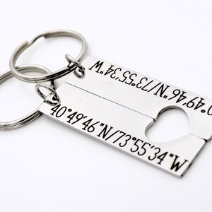 May include: Two silver keychains with a heart-shaped cutout. The keychains are engraved with the coordinates 40&deg;49&prime;46&Prime;N/73&deg;55&prime;34&Prime;W.