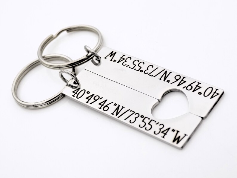 May include: Two silver keychains with a heart-shaped cutout. The keychains are engraved with the coordinates 40&deg;49&prime;46&Prime;N/73&deg;55&prime;34&Prime;W.