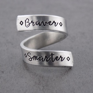 May include: A silver ring with the words "Braver" and "Smarter" engraved on it. The ring is twisted into a spiral shape.