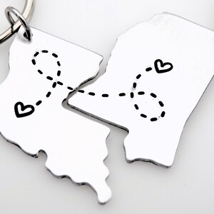 May include: Two silver keychains shaped like a state outline, connected by a dotted line with hearts at each end. The keychains are meant to be separated and given to two people.