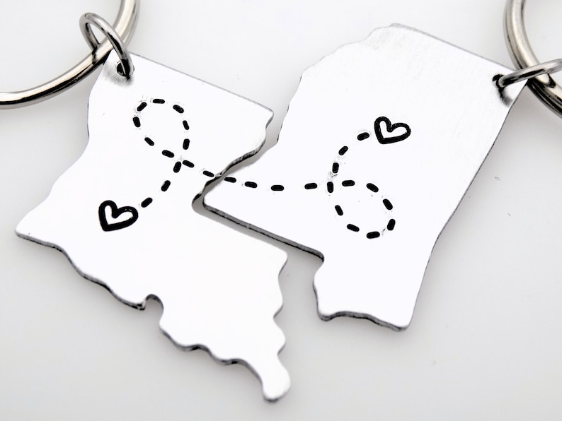May include: Two silver keychains shaped like a state outline, connected by a dotted line with hearts at each end. The keychains are meant to be separated and given to two people.