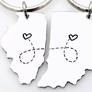 May include: Two silver keychains shaped like the states of Illinois and Indiana, connected by a dashed line with hearts at each end.