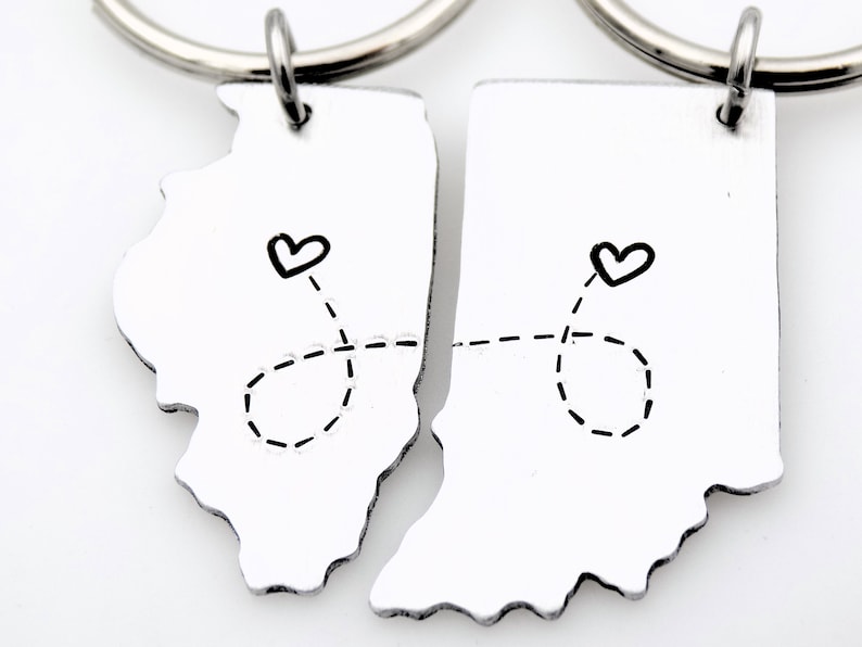 May include: Two silver keychains shaped like the states of Illinois and Indiana, connected by a dashed line with hearts at each end.