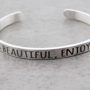 May include: Silver bangle bracelet with the inscription "Life is beautiful, enjoy the ride".
