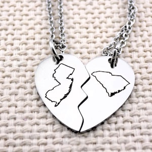 May include: Two silver necklaces with heart-shaped pendants. Each pendant is half of a heart and features the outline of a state. One pendant features the outline of New Jersey and the other features the outline of South Carolina.