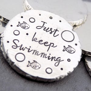 May include: A silver charm with the text "Just keep swimming" and a design of fish and bubbles.