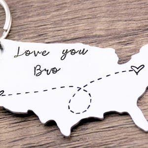 May include: A silver keychain shaped like the United States with a dashed line connecting two hearts. The keychain has the text "Love you Bro" engraved on it.