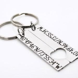 May include: A silver keychain with two key rings and a rectangular tag split in half. The tag has the coordinates "40&deg;49&prime;46&Prime;N/73&deg;55&prime;34" on one side and "40&deg;49&prime;46&Prime;N/73&deg;55&prime;34&Prime;W" on the other side, with a heart-shaped cutout in the middle.