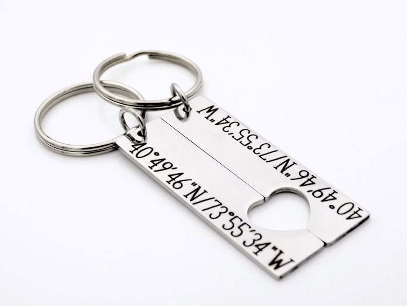 May include: A silver keychain with two key rings and a rectangular tag split in half. The tag has the coordinates "40&deg;49&prime;46&Prime;N/73&deg;55&prime;34" on one side and "40&deg;49&prime;46&Prime;N/73&deg;55&prime;34&Prime;W" on the other side, with a heart-shaped cutout in the middle.
