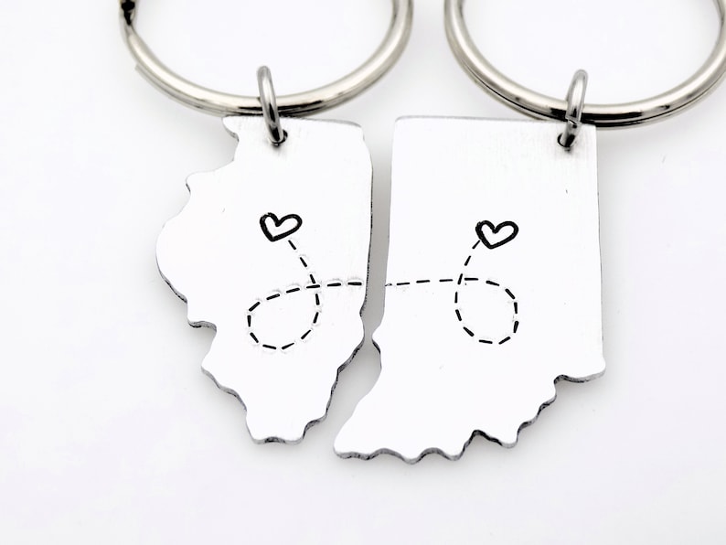 May include: Two silver keychains shaped like the states of Illinois and Indiana, connected by a dashed line with hearts at each end. The keychains are a gift for a couple who live in different states.