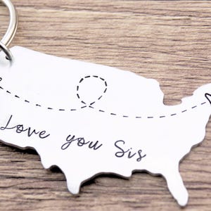 May include: Silver keychain shaped like the United States with a dashed line connecting two hearts and the text "Love you Sis".