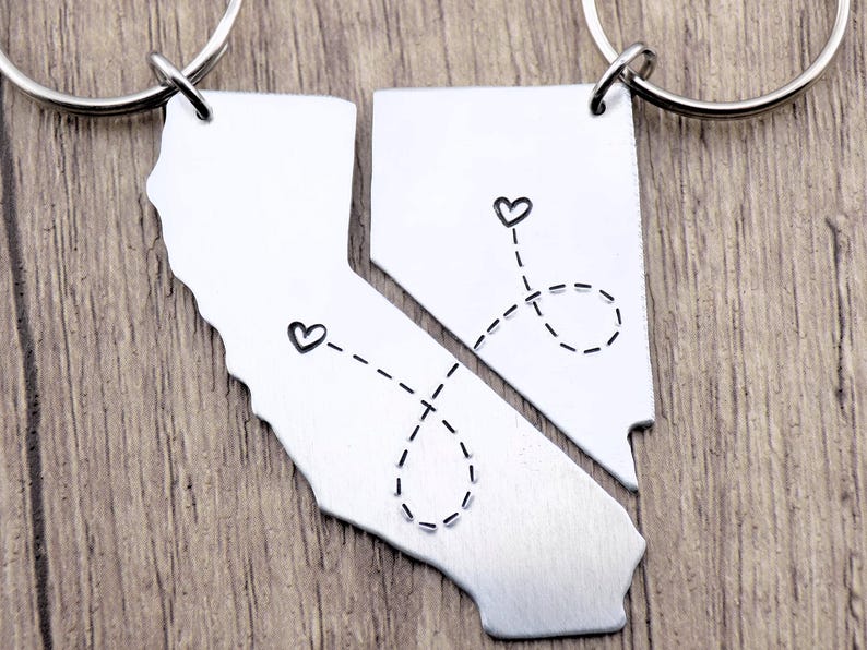 May include: Two silver keychains shaped like the state of California, with a dotted line connecting two hearts on each keychain. The keychains are separated, suggesting a long-distance relationship.