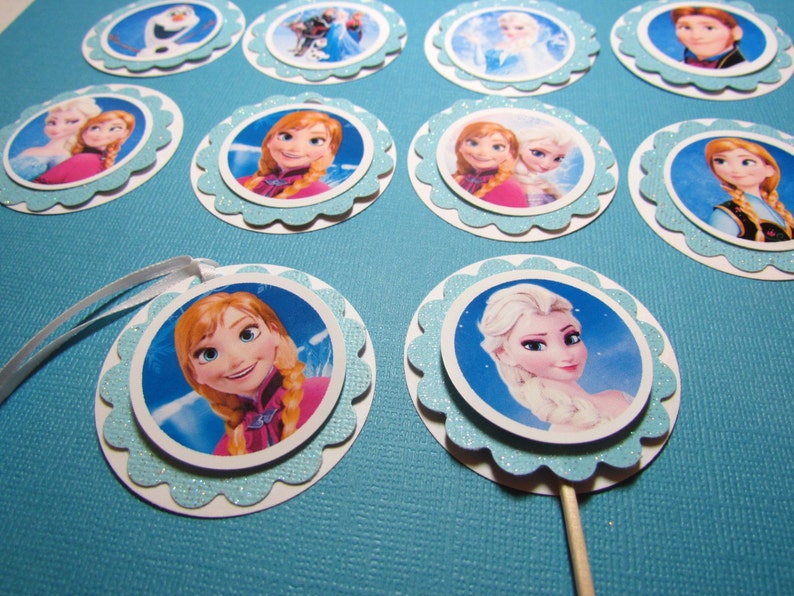 Puede incluir: Un conjunto de 10 adornos redondos para cupcakes con personajes de la pel&iacute;cula animada Frozen. Los adornos est&aacute;n impresos en cartulina blanca con un borde azul brillante y presentan im&aacute;genes de Elsa, Anna, Olaf y Kristoff.