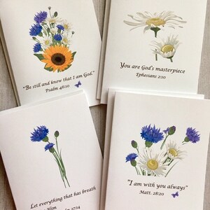 May include: Set of eight blank greeting cards featuring floral designs and inspirational quotes. Each card has a different flower arrangement and a Bible verse. The cards are white with a subtle texture.