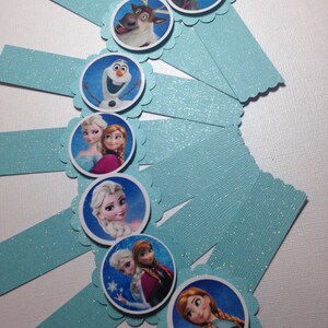 Puede incluir: Conjunto de ocho envoltorios para cupcakes de purpurina azul con bordes redondeados y festoneados. Cada envoltorio presenta un personaje diferente de la pel&iacute;cula animada Frozen, incluyendo Elsa, Anna, Olaf, Kristoff y Sven.