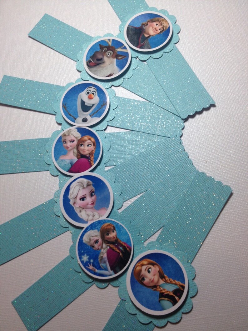 Puede incluir: Conjunto de ocho envoltorios para cupcakes de purpurina azul con bordes redondeados y festoneados. Cada envoltorio presenta un personaje diferente de la pel&iacute;cula animada Frozen, incluyendo Elsa, Anna, Olaf, Kristoff y Sven.