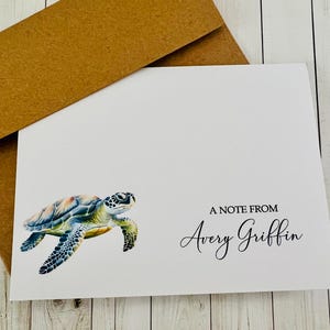 May include: White stationery card with a watercolor sea turtle illustration and a brown envelope. The card reads "A NOTE FROM Avery Griffin" in elegant script. The turtle features shades of blue, green, and yellow.