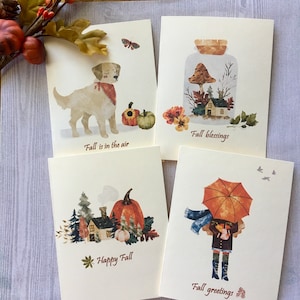 May include: Set of four fall-themed greeting cards. Each card features watercolor illustrations of autumn scenes, including a dog, pumpkins, a house, and a person with an umbrella. The cards have text that reads "Fall is in the air", "Fall blessings", "Happy Fall", and "Fall greetings".
