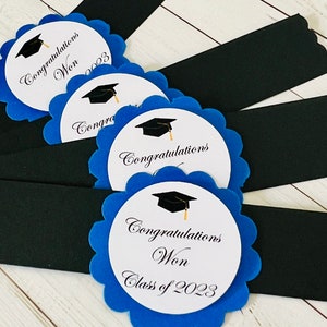 May include: Four blue and white graduation party favor tags with black graduation caps and the text "Congratulations Won Class of 2023".