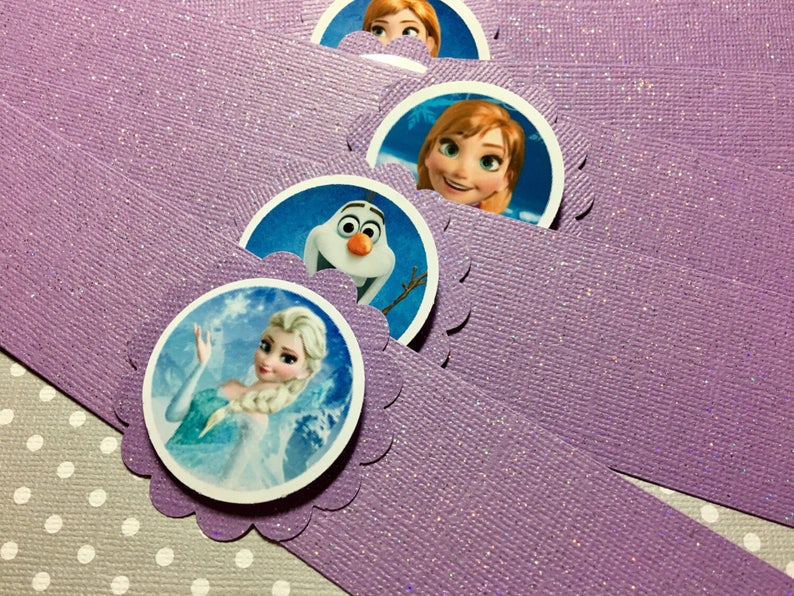 Puede incluir: Anillos de servilleta de papel morado con purpurina y bordes redondeados y festoneados. Cada anillo presenta un personaje diferente de la pel&iacute;cula Frozen: Elsa, Anna y Olaf.