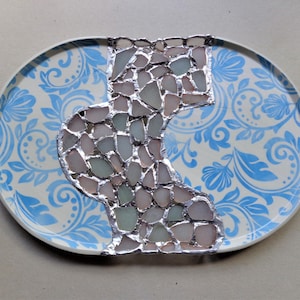 May include: Oval decorative plate with a blue and white floral pattern. A mosaic design of sea glass in shades of pink, green, and gray is set in the center of the plate, creating a unique artistic accent.