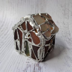 Puede incluir: Una casa en miniatura hecha a mano con un marco de metal plateado. La casa presenta un mosaico de piezas de vidrio marrón, beige y verde. El techo es de vidrio de color claro. Es un objeto decorativo.