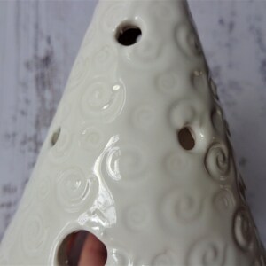 May include: Cream-colored ceramic Christmas tree with a glossy finish. The tree features a spiral pattern and several circular openings. A decorative item for the holiday season.