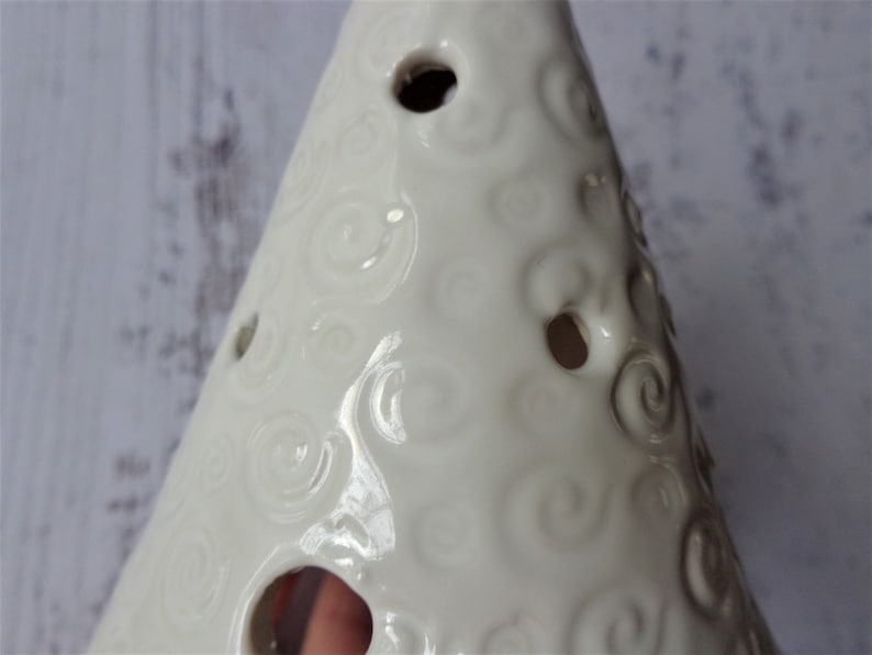 May include: Cream-colored ceramic Christmas tree with a glossy finish. The tree features a spiral pattern and several circular openings. A decorative item for the holiday season.