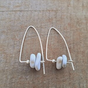 May include: A pair of silver drop earrings. Each earring has a curved wire design, a small, round bead, and three pale blue, oblong beads. The earrings are presented on a wooden surface.