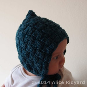 May include: A teal blue knitted baby bonnet with a pointed top and a tie under the chin. The bonnet is made with a textured stitch pattern.