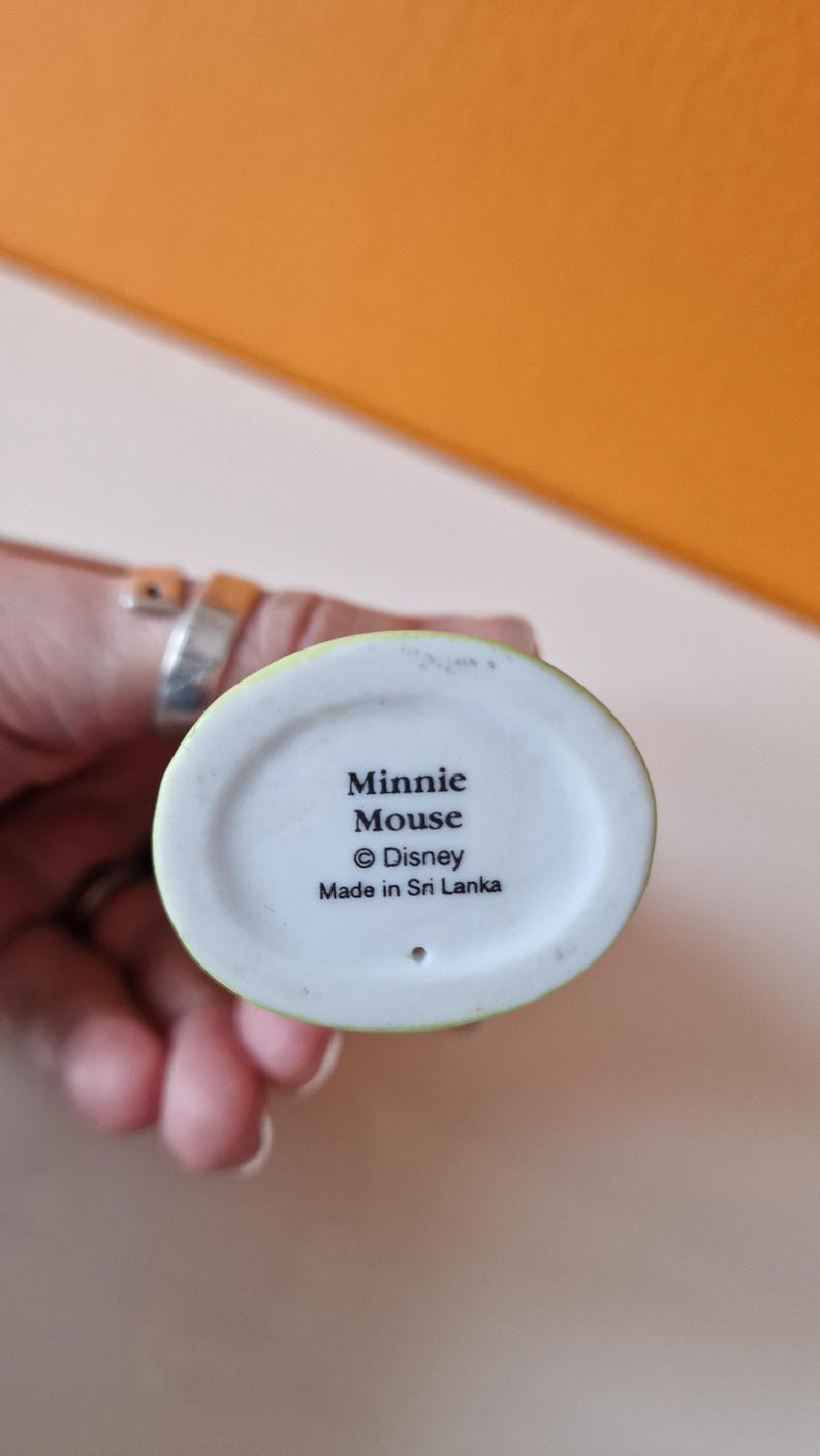 May include: A white ceramic figurine of Minnie Mouse with a green base. The base has the text "Minnie Mouse &copy; Disney Made in Sri Lanka".